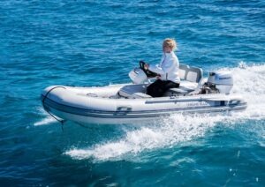 A person driving a Pearl 62 inflatable boat on clear blue water, 2022 model.