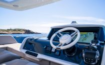 Helm of 2022 Pearl 62 yacht with navigation display, steering wheel, and ocean view.