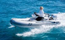 A person driving a Pearl 62 inflatable boat on clear blue water, 2022 model.