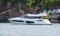 2021 Sunseeker Manhattan 68 yacht cruising near rocky coastline and houses.